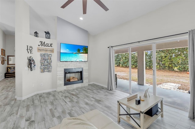 living room with ceiling fan, high vaulted ceiling, a fireplace, and light hardwood / wood-style flooring