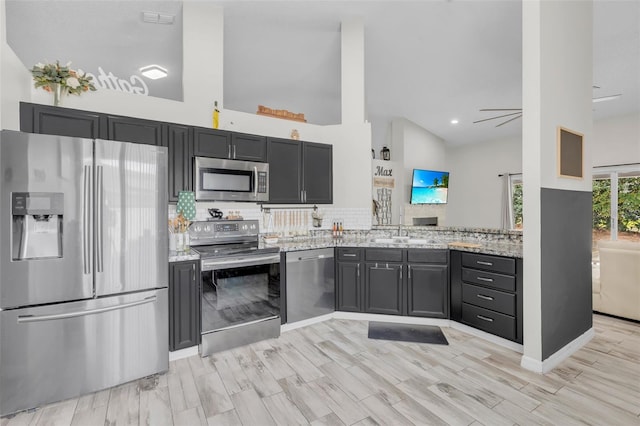 kitchen with high vaulted ceiling, ceiling fan, light stone counters, and stainless steel appliances