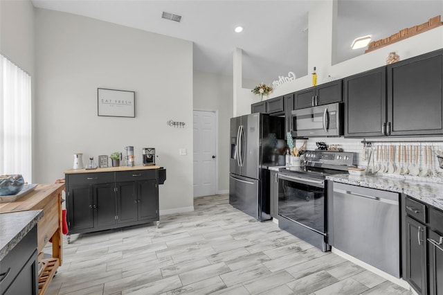 kitchen with light stone counters, decorative backsplash, appliances with stainless steel finishes, and a towering ceiling