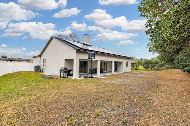 rear view of house featuring a lawn, central air condition unit, solar panels, and a patio