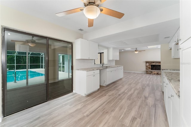 kitchen with light stone countertops, white cabinets, light hardwood / wood-style flooring, and a fireplace