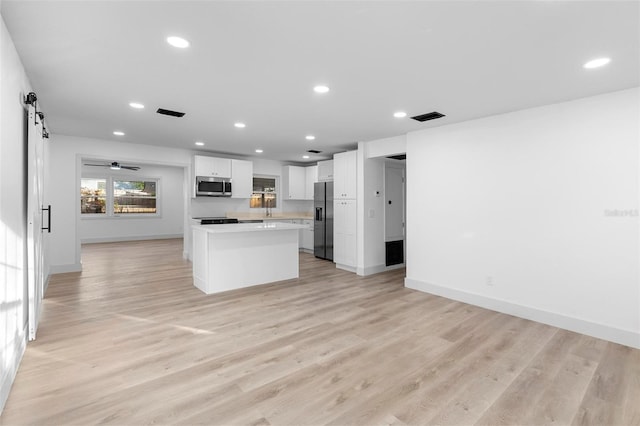 kitchen featuring white cabinets, a center island, stainless steel appliances, light hardwood / wood-style flooring, and a barn door