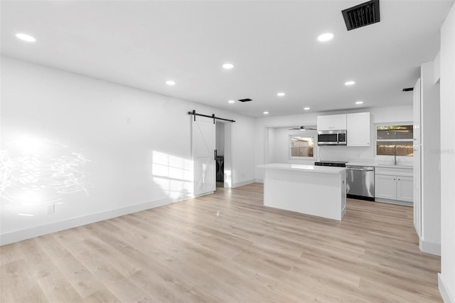 kitchen with a barn door, appliances with stainless steel finishes, light wood-type flooring, a kitchen island, and white cabinets