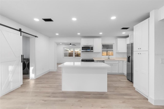 kitchen featuring a barn door, stainless steel appliances, washing machine and dryer, white cabinets, and sink