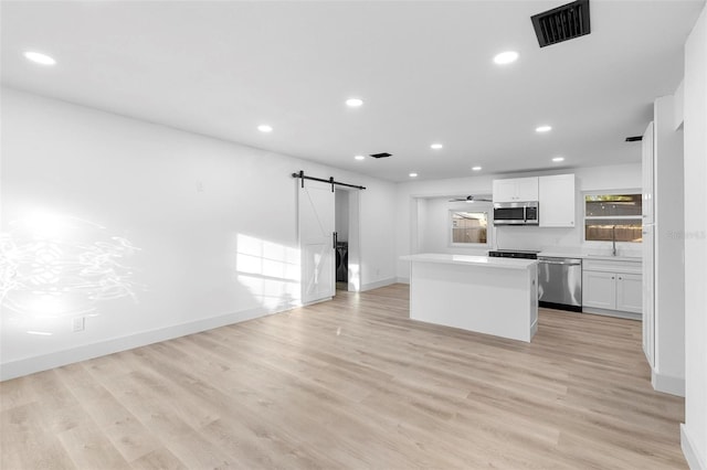 kitchen with a barn door, a center island, stainless steel appliances, white cabinets, and visible vents