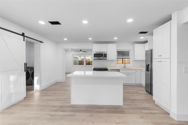 kitchen featuring a barn door, stainless steel appliances, a sink, independent washer and dryer, and a kitchen island