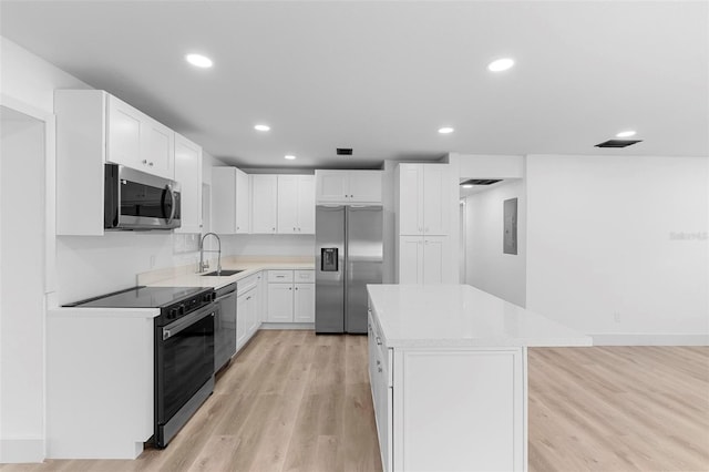 kitchen featuring a center island, a sink, stainless steel appliances, light wood finished floors, and white cabinetry