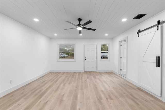 interior space with light wood finished floors, a barn door, visible vents, a ceiling fan, and wood ceiling