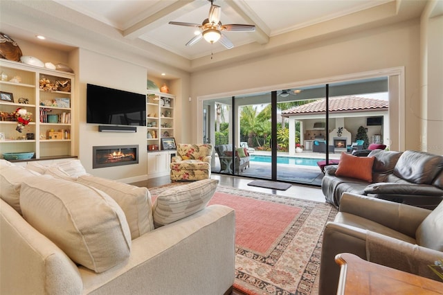 living room featuring ceiling fan, built in features, beam ceiling, and ornamental molding