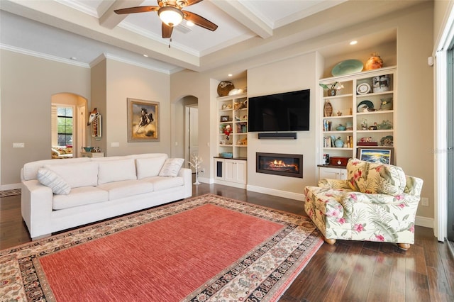 living room with ceiling fan, dark hardwood / wood-style flooring, crown molding, beam ceiling, and built in shelves