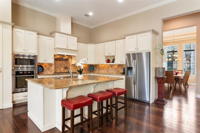 kitchen featuring appliances with stainless steel finishes, light stone counters, tasteful backsplash, and an island with sink