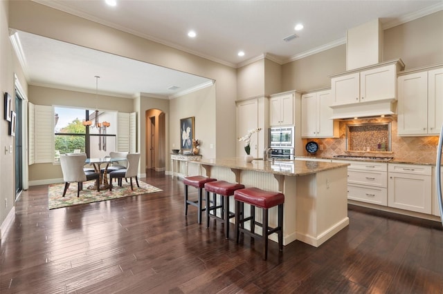 kitchen with decorative backsplash, a kitchen bar, an island with sink, stainless steel appliances, and light stone counters