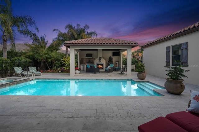 pool at dusk featuring an outdoor fireplace, a patio, and an in ground hot tub