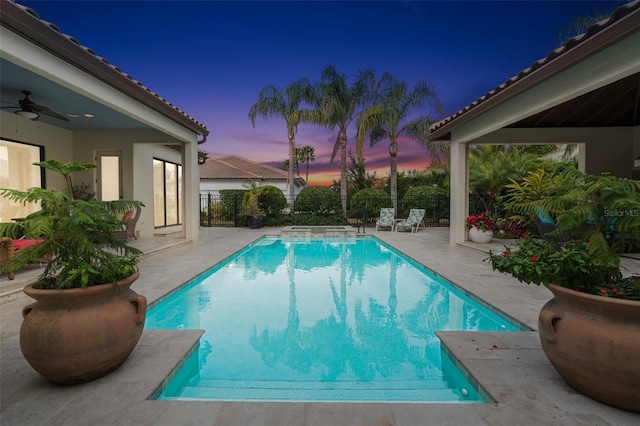 pool at dusk with ceiling fan and a patio