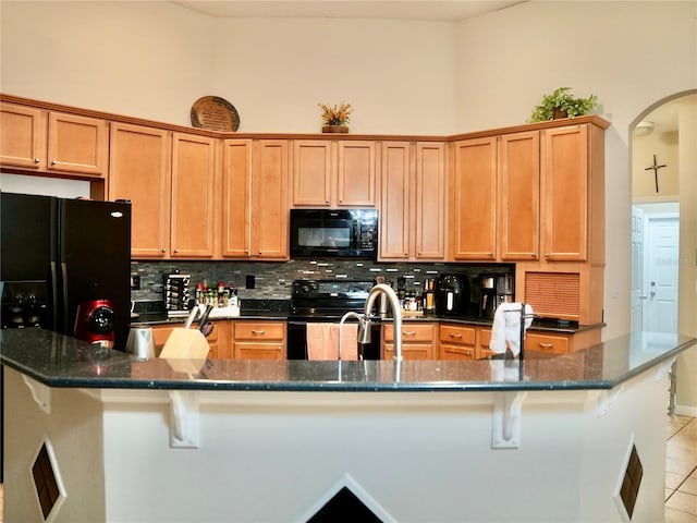 kitchen featuring black appliances, light tile patterned floors, an island with sink, dark stone counters, and backsplash