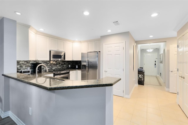 kitchen with backsplash, stainless steel appliances, white cabinets, kitchen peninsula, and dark stone counters