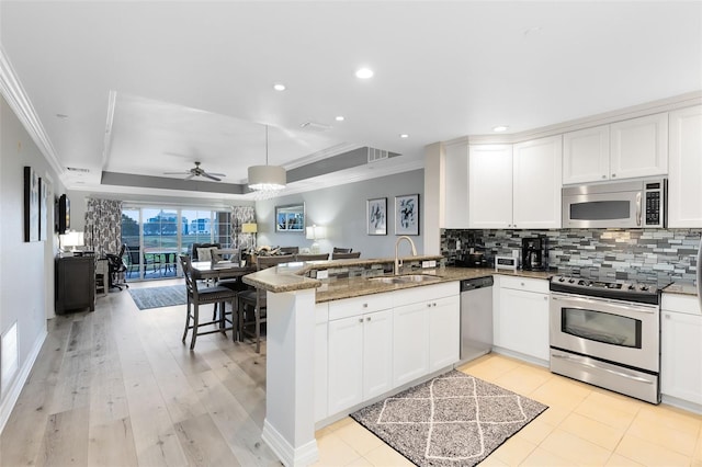 kitchen with sink, dark stone countertops, white cabinets, kitchen peninsula, and stainless steel appliances