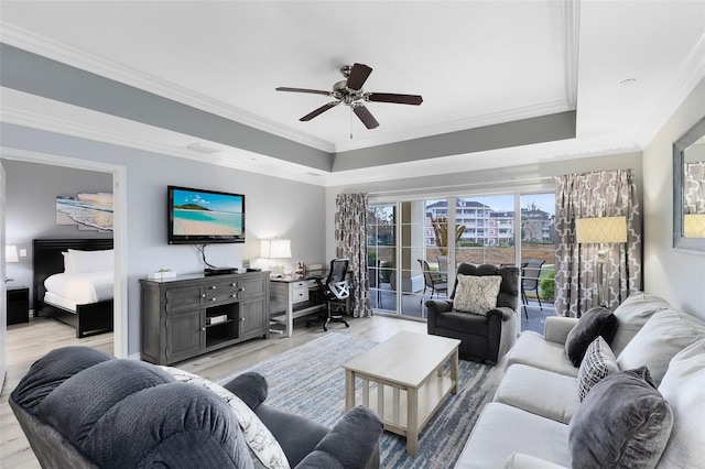 living room with ceiling fan, ornamental molding, a raised ceiling, and light wood-type flooring
