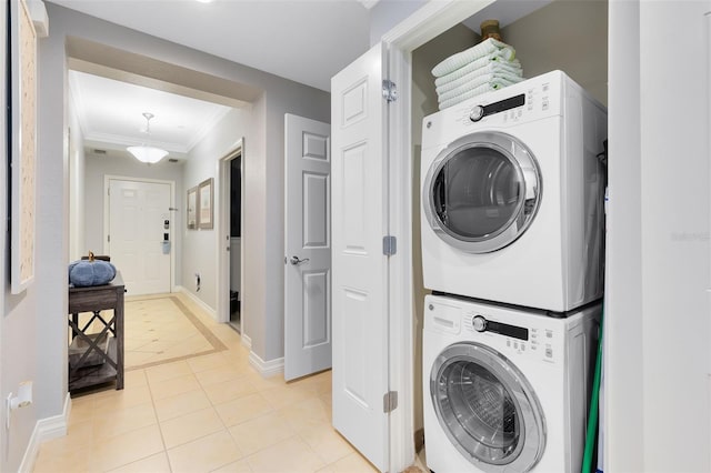 clothes washing area featuring crown molding, stacked washer / drying machine, and light tile patterned floors