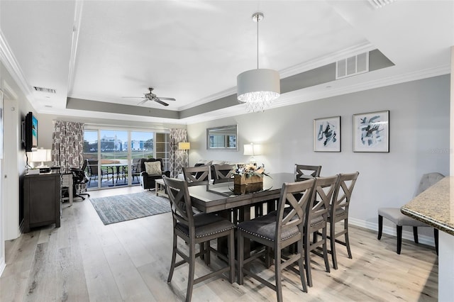 dining area with ceiling fan with notable chandelier, ornamental molding, a raised ceiling, and light hardwood / wood-style floors
