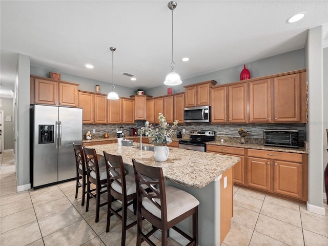 kitchen featuring appliances with stainless steel finishes, an island with sink, hanging light fixtures, a breakfast bar, and light tile patterned floors