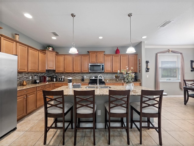 kitchen with a kitchen island with sink, sink, stainless steel appliances, and pendant lighting