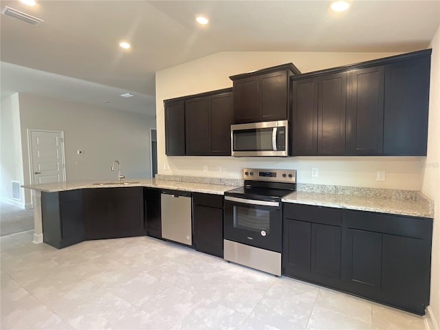 kitchen with vaulted ceiling, kitchen peninsula, sink, appliances with stainless steel finishes, and light stone counters