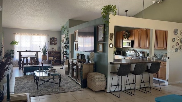 kitchen with vaulted ceiling, light tile patterned flooring, a textured ceiling, and appliances with stainless steel finishes