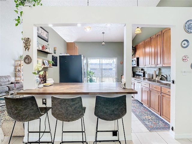 kitchen featuring sink, light tile patterned floors, a breakfast bar, appliances with stainless steel finishes, and butcher block counters