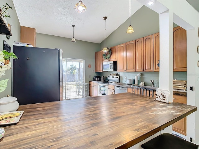 kitchen with butcher block counters, vaulted ceiling, hanging light fixtures, a textured ceiling, and appliances with stainless steel finishes