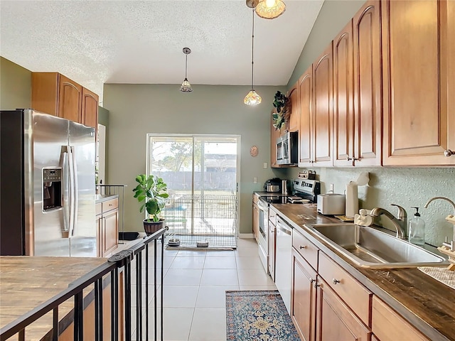 kitchen featuring sink, a textured ceiling, light tile patterned floors, appliances with stainless steel finishes, and pendant lighting