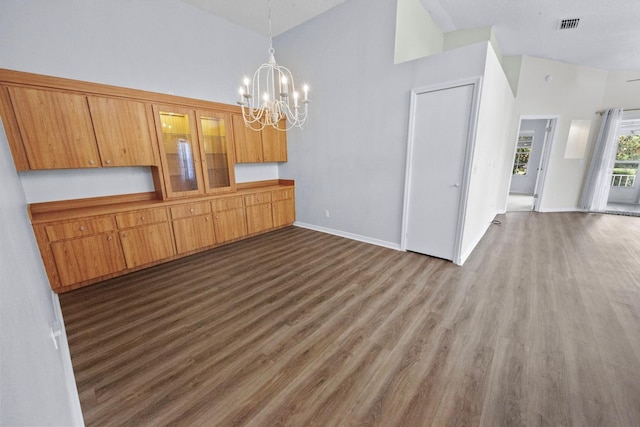 unfurnished dining area featuring an inviting chandelier, dark hardwood / wood-style flooring, and high vaulted ceiling