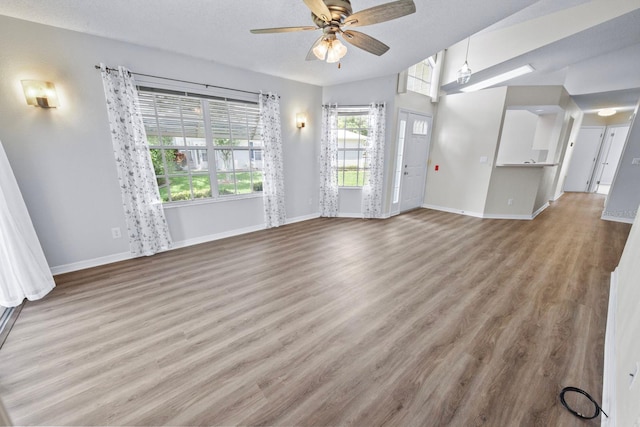 unfurnished living room featuring ceiling fan, vaulted ceiling, a textured ceiling, and light wood-type flooring