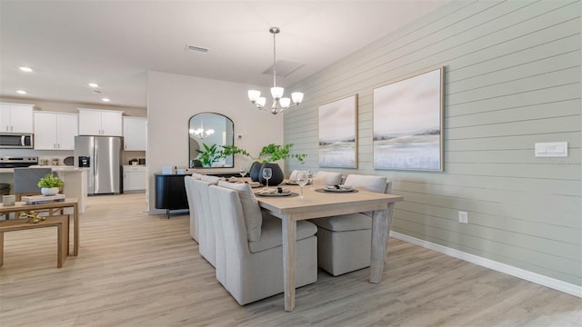 dining area featuring an inviting chandelier, light hardwood / wood-style floors, and wooden walls