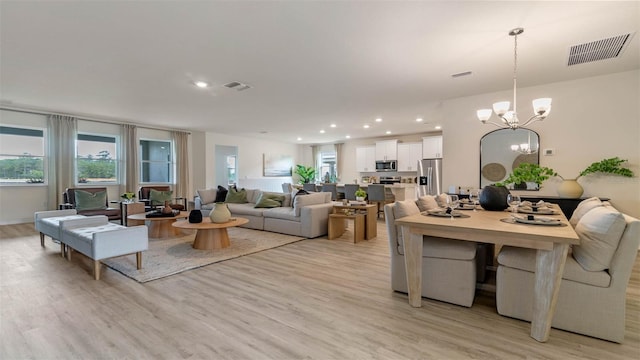 living room with an inviting chandelier, a wealth of natural light, and light hardwood / wood-style floors