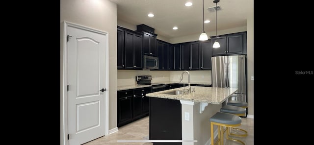 kitchen with light stone countertops, pendant lighting, stainless steel appliances, an island with sink, and sink