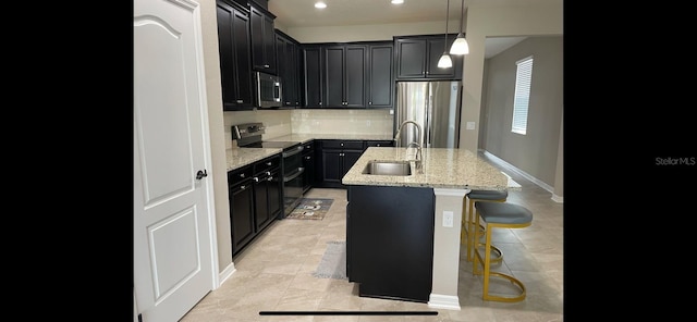 kitchen featuring a center island with sink, a kitchen bar, sink, stainless steel appliances, and light stone counters