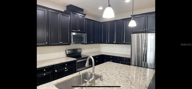 kitchen with appliances with stainless steel finishes, hanging light fixtures, a textured ceiling, light stone counters, and sink