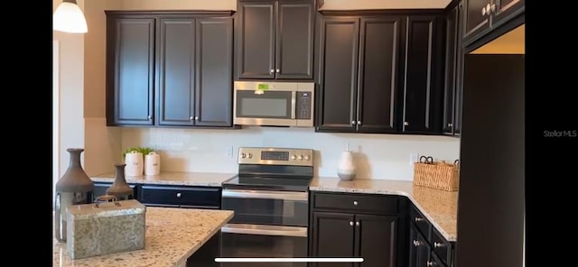 kitchen featuring hanging light fixtures, dark brown cabinets, light stone counters, and stainless steel appliances