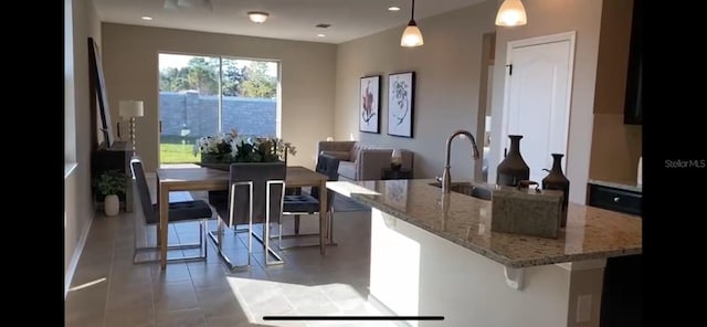 kitchen with decorative light fixtures, tile patterned floors, sink, a kitchen breakfast bar, and light stone counters