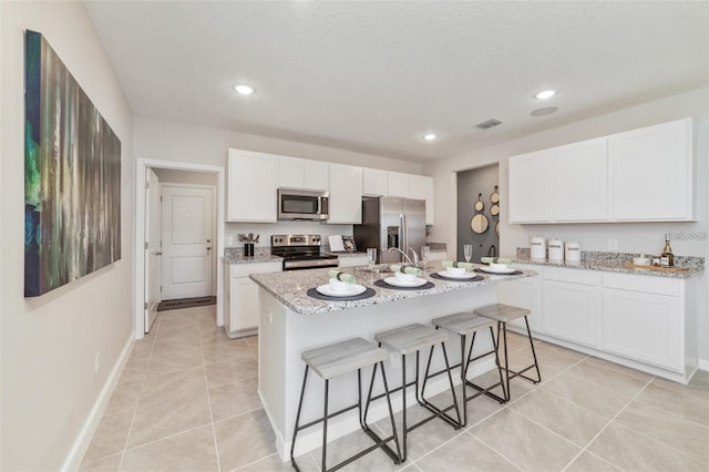 kitchen featuring a kitchen breakfast bar, white cabinetry, light stone countertops, a kitchen island with sink, and stainless steel appliances