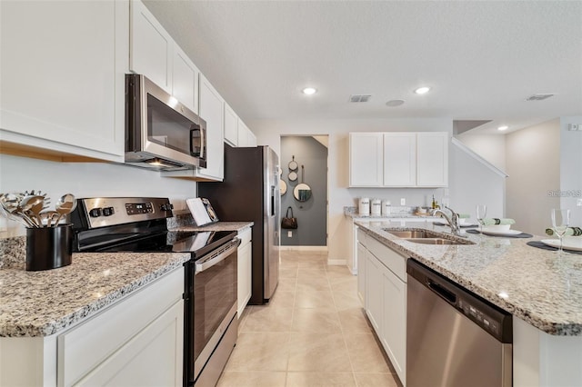 kitchen with appliances with stainless steel finishes, sink, white cabinets, light tile patterned floors, and light stone counters