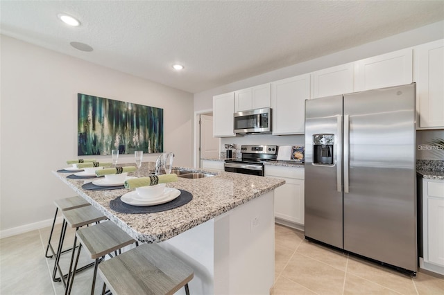 kitchen featuring light stone countertops, appliances with stainless steel finishes, sink, white cabinets, and a breakfast bar area