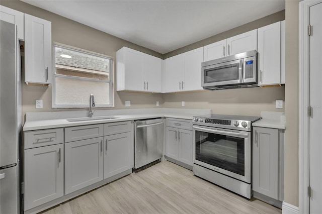 kitchen with stainless steel appliances, sink, white cabinets, and light hardwood / wood-style floors