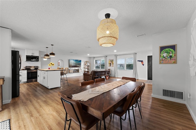 dining area with a textured ceiling and light hardwood / wood-style flooring