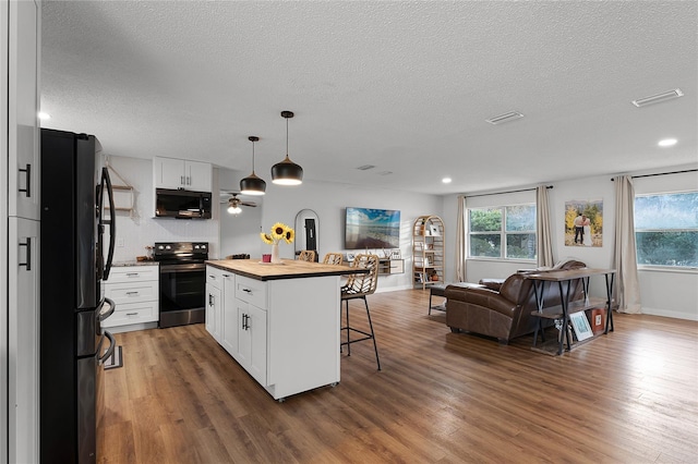 kitchen with white cabinets, a kitchen island, black refrigerator, a kitchen breakfast bar, and stainless steel range with electric stovetop