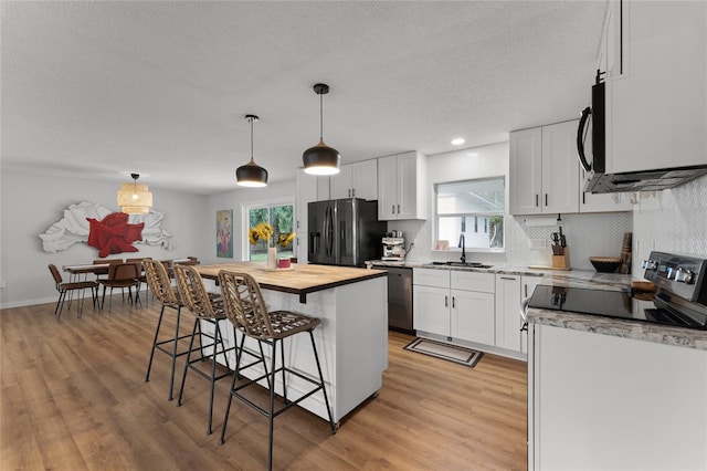 kitchen with black fridge, a kitchen island, white cabinets, and decorative light fixtures