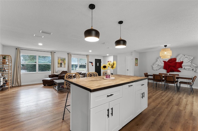 kitchen with a kitchen island, a kitchen bar, wood counters, white cabinetry, and hanging light fixtures