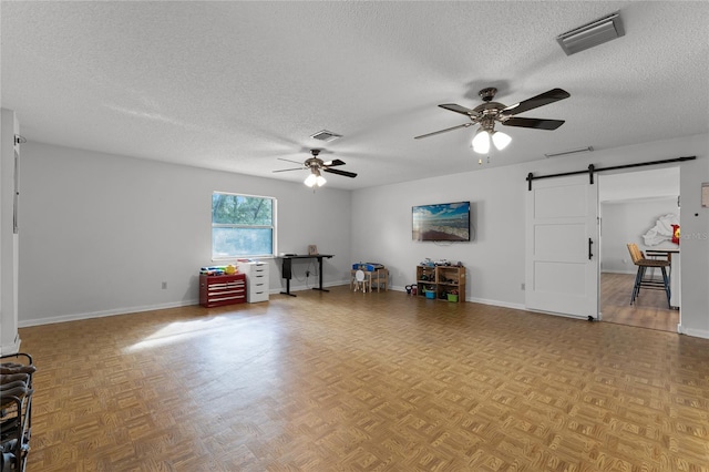 living room with a textured ceiling, ceiling fan, a barn door, and light parquet flooring