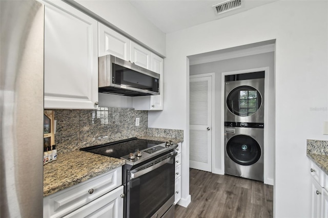 kitchen featuring stone counters, stainless steel appliances, stacked washer and clothes dryer, and white cabinetry